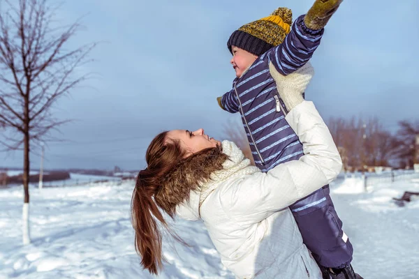 Mutter mit kleinem Sohn 3 Jahre alt, sonniger Tag im Winter draußen im Park. Spielen an der frischen Luft. eine glücklich lächelnde junge Frau amüsiert sich mit einem Jungen. das Konzept der Flucht des Kindes. — Stockfoto