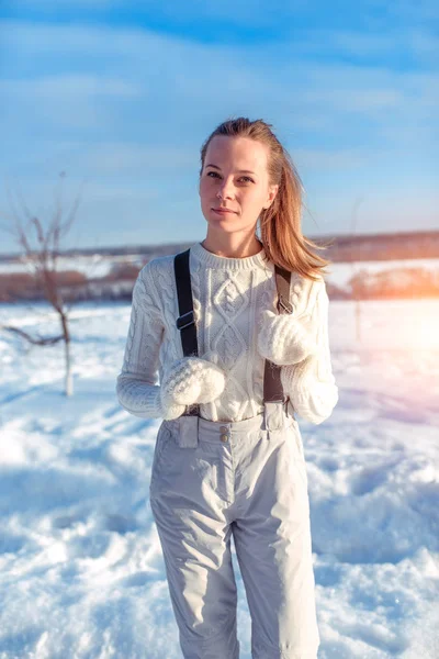 Vacker kvinna i en vit jumpsuit tröja och vantar. Poserar mot bakgrund av snöiga väder. Happy vila i frisk luft. — Stockfoto