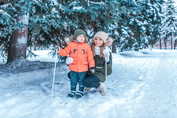 Seorang ibu muda mengajari anaknya 3-5 tahun untuk bermain ski. Di musim dingin di hutan di mana ada banyak salju. Happy friends cuti pada akhir pekan . — Stok Foto