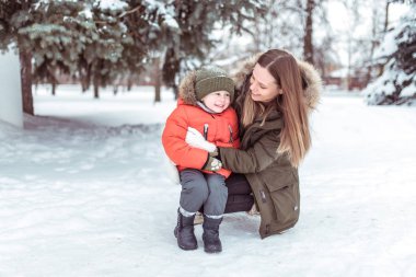 Küçük çocuk 3-5 yaşında, bir çocuk kışın sıcak ceket ve şapka. Kışın, karda yeşil Noel ağaçları çerçevede bir. Anne ile oğlu doğada çalış. Mutlu karlı ormanda gülümseyen.
