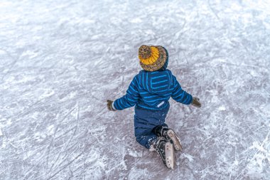 Küçük çocuk çocuk 3-5 yıl eski, karla kaplı buz paten üzerinde oturuyor. Buz pateni için kışın sitede şehirde. Metin için boş alan.