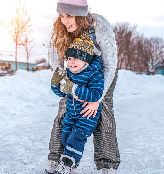 Rapariga segura um rapazinho. No inverno, patine na cidade. Vista frontal. Irmã com seu filho aprende a patinar e ficar de patins . — Fotografia de Stock