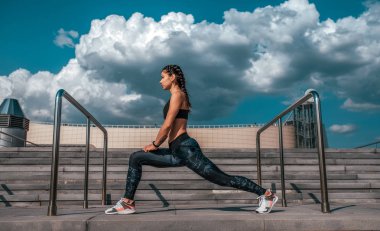 Sporcu kız şehirde sabah koşu önce germe yapıyor. Beton merdiven ve bulutlar arka planı. Sağlıklı bir yaşam tarzı kavramı. Spor giyim ve spor ayakkabı.
