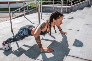 Kız atlet merdivenlerde şehirde sabah bastırdı. Isınma Jimnastik yapar. Sağlıklı bir yaşam tarzı kavramı. Spor giyim ve spor ayakkabısı. Tabaklanmış deri ve dövmeler.