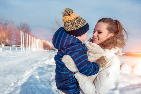 Jonge moeder glimlacht gelukkig, houdt in haar armen een jongen van 2-5 jaar oud, in de winter buiten spelen. Rust in de winterochtend in de natuur. — Stockfoto