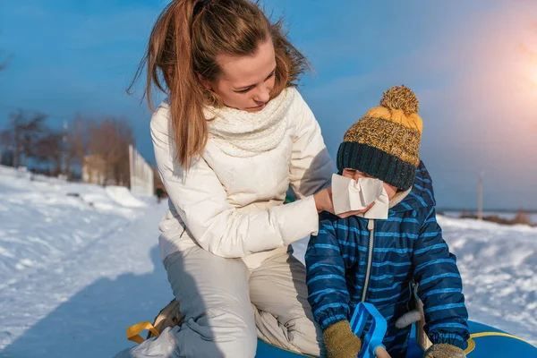 Jonge moeder veegt snot haar baby. In de winter in de frisse lucht. Het concept van ouder- en ziekenzorg. Loopneus, verkoudheid en verstopte neus. — Stockfoto
