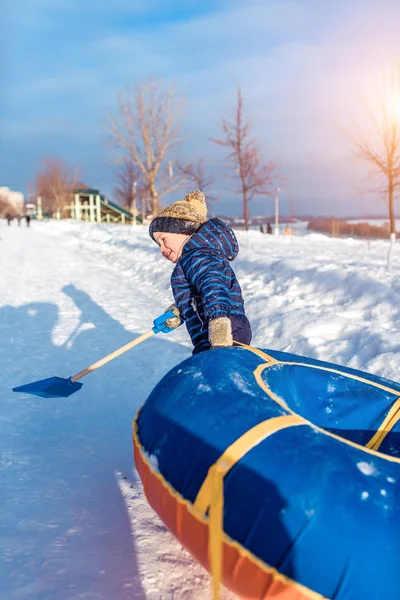 Küçük çocuk tüp çeker. Bir spatula Holding'in elinde. Kışın, şehrin bir roller coaster üzerinde mutlu bir çocuk çalış.