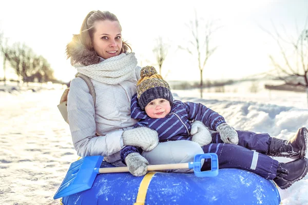 Glücklich lächelnd sitzt die junge Mutter mit ihrem vier- bis fünfjährigen Sohn auf Schläuchen und spielt im Winter Scrabbeln. Ruhe am Wintermorgen in der Natur. — Stockfoto