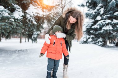 Anne bir mitten ile onun oğlu Çocuk sümüklü mendil. Burnu tıkalı olan bir bebek bakımı. Kışın ortasında yeşil firs parkta.