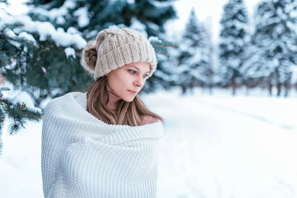 Ritratto di ragazza nella foresta invernale su sfondo di alberi innevati. In un plaid bianco e cappello bianco. Spazio libero per il testo. Sullo sfondo di una foresta verde . — Foto Stock