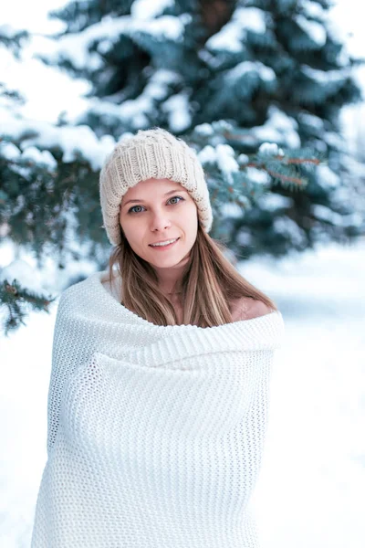 Portrét dívky v zimním lese na pozadí zasněžených stromů. Bílý pléd a bílý klobouk. Krásná žena v sadech v zimě. — Stock fotografie