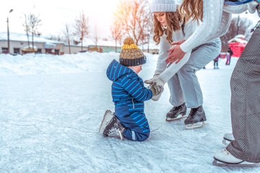Anne Çocuk yükselmeye yardımcı olur. Kaymak 3-6 yaşında küçük bir çocuk öğrenir. Dizlerinin üzerine düştü. Kışın şehir pisti üzerinde. Bir sıcak şapka ve mavi tulum.