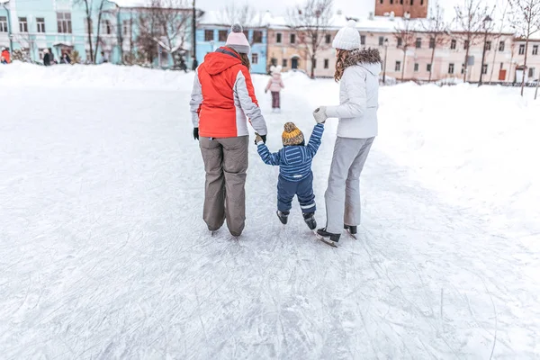 Two young mothers learn to skate small child boy 3-4 years old. In winter, ice skating on the ice in the city.