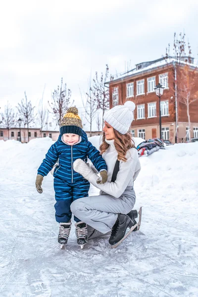 4-6 éves kisfiú korcsolyázás. Boldog, mosolyog, anya tartja a fiát, segít, hogy felfüggeszti. első lépések a korcsolyát. Télen a jégpálya a város. — Stock Fotó