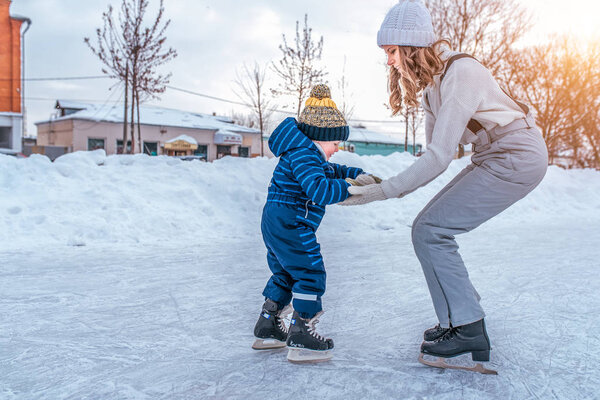 A little boy of 3-5 years old is skating. Mom keeps her son helps to resist. First steps on skates. In the winter in city on the rink. The concept of support and support in education of children.