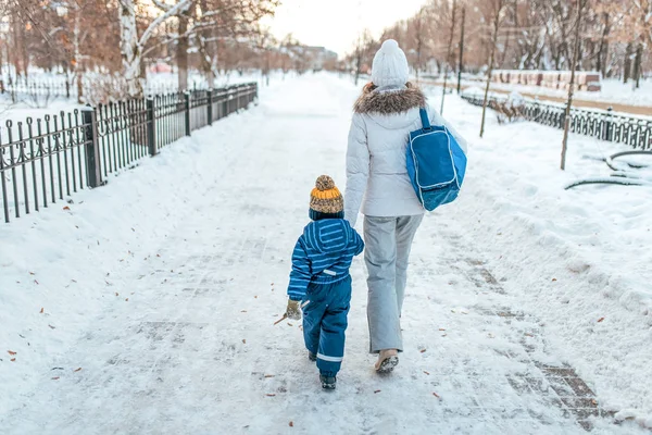 年轻的母亲和她的小男孩儿子手拉手。在冬天在城市在新鲜空气。照顾和照顾孩子的概念, 护送到幼儿园. — 图库照片
