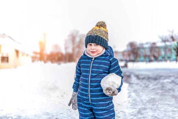 Seorang anak laki-laki berusia 3-6 tahun berdiri di luar di musim dingin di kota. Di tangan memegang bola salju besar. Ruang kosong untuk teks. Permainan anak-anak di musim dingin . — Stok Foto