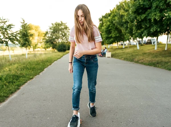 Gadis remaja berusia 11-13 tahun, di musim panas di kota, mengendarai skateboard. Rambut panjang, beristirahat di taman setelah pelajaran . — Stok Foto