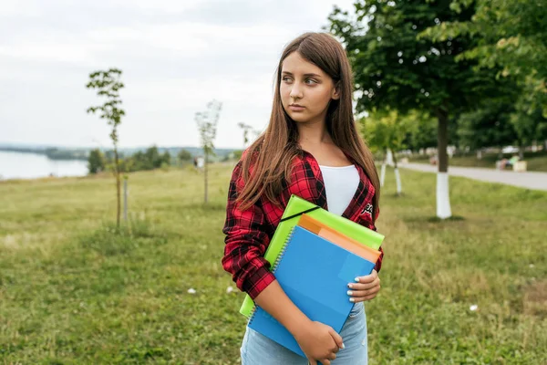 Chica adolescente en el verano en el parque, con una camisa roja en las manos sosteniendo cuadernos y notas para la escuela . — Foto de Stock