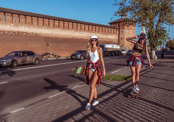 Zwei Mädchen fahren, Freundinnen im Sommer in der Stadt unterwegs. mit Longboard-Skateboard, Sonnenbrille. Spaß auf dem Bürgersteig. Freiraum für Text. — Stockfoto