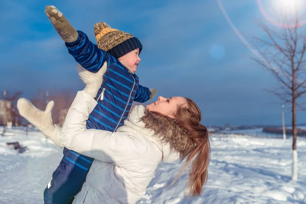 Junge Frau Mutter spielt Flugzeuge mit Kind Junge. im Winter im Stadtpark auf der Straße. glücklich lächelnd. in Freizeitkleidung. Freiraum für Text. — Stockfoto