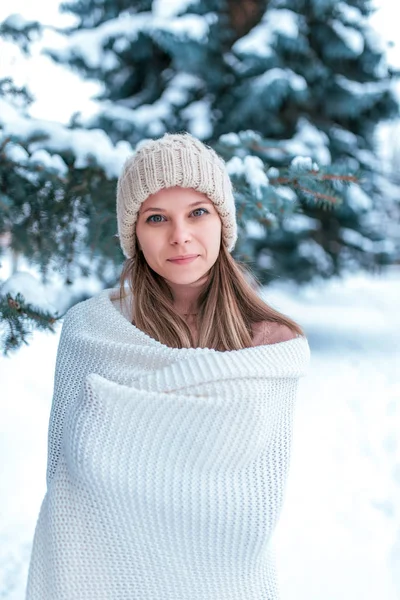 흰 모자와 격자 무늬, 행복 한 미소에 여자의 초상화. 크리스마스 나무의 배경에 눈 덮인 숲에서 캠핑 여성. 따뜻한 담요에 싸여. — 스톡 사진