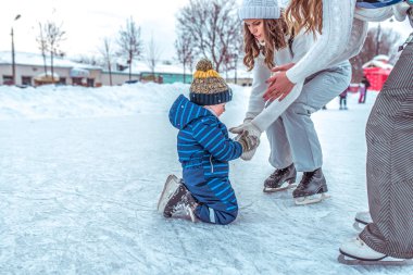 Genç bir anne kız arkadaşıyla el ile küçük çocuk 2-4 yaşında çocuk ayağa yardımcı olur. Kış City pisti. Geri kalanı temiz hava. Paten, yardım ve destek ana ilk adımları. Metin için boş alan.