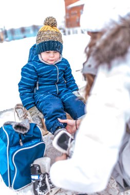 Genç bir anne paten üzerinde koyar, 2-4 yaşında çocuk küçük bir çocuk yardımcı olur. Kışın şehir pisti üzerinde. Paten taze soğuk havada üzerine getirin. Bir çocuk, yardım ve destek ana kadın ayakkabı.