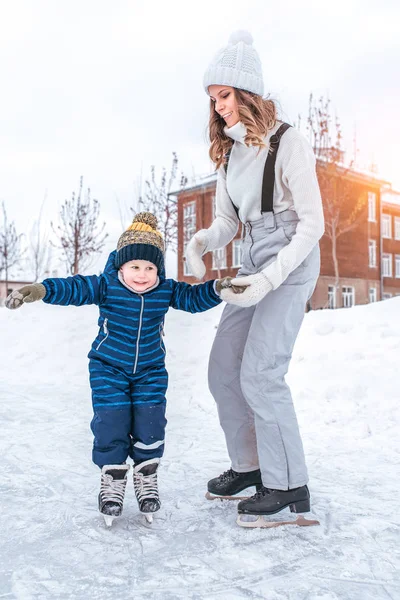 一位年轻的母亲牵着一个4-5 小孩的手。冬天, 在城市的溜冰场上。您可以在新鲜的冷风中放松身心。与婴儿在温暖的衣服的妇女. — 图库照片