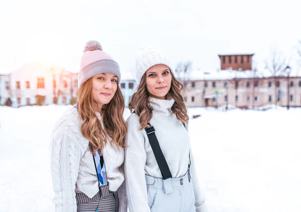Dua gadis cantik pacar, perempuan berpose bahagia di musim dingin di kota. Dalam pakaian hangat putih kasual dan topi. Ruang kosong untuk teks. Istirahat di hari musim dingin di latar belakang snowdrifts . — Stok Foto