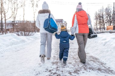 Anne ve kız sokakta yürürken el tarafından çocuk s oğlu 3-5 yaşında görür. Arkadan görünüm. Kış City snowdrifts arka plan üzerinde. Olaydan eve dönüyoruz. İki kadın kız, Anne.
