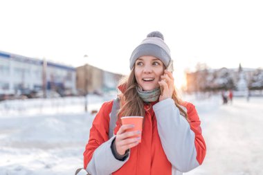 Genç bir kız telefonla çağırır. Mutlu neşeli merak ediyorum. İçinde şehirde elinde bir bardak kahve kış. Elinde bir smartphone. Sürpriz ve bir kadının yüzünde zevk duygular.