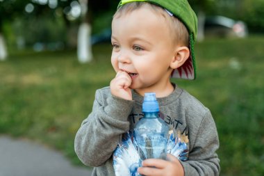 Küçük çocuk çocuk 2-3 yıl eski, yakın çekim portre, mutlu elinde bir şişe su tutarak gülüyor. Temiz havada şehirde yazları. Samimi ve şaşırmış gibi bakıyorsun.