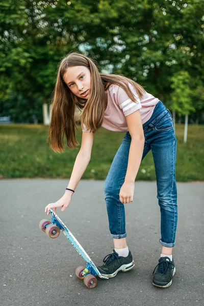 Gadis remaja 9-11 tahun, naik skateboard. Di musim panas di kota dengan celana jeans dan sepatu olahraga . — Stok Foto