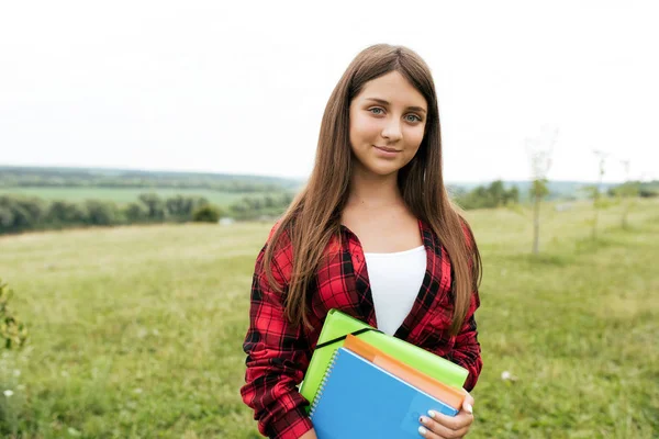 Une adolescente de 10 à 13 ans se tient dans un parc en été sur fond de prairies verdoyantes et de champs. Dans les mains de tenir des carnets et des dossiers de documents dans le parc de la ville . — Photo