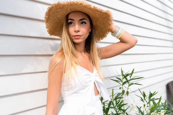 Mooi meisje in een stro hoed op een houten witte muur achtergrond. Vrouw in jurk met gebruinde huid en dagelijkse make-up. In de zomer op het terras van de zon. — Stockfoto