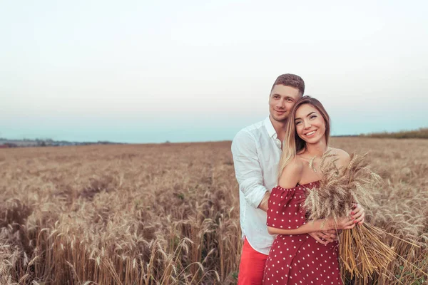 Pareja joven hombre y mujer en el campo de trigo de verano, abrazándose y relajándose al aire libre. El concepto de amor alegría y relación de cuidado. Romántico encuentro amanecer y atardecer. Texto de espacio libre. En las manos trigo . — Foto de Stock