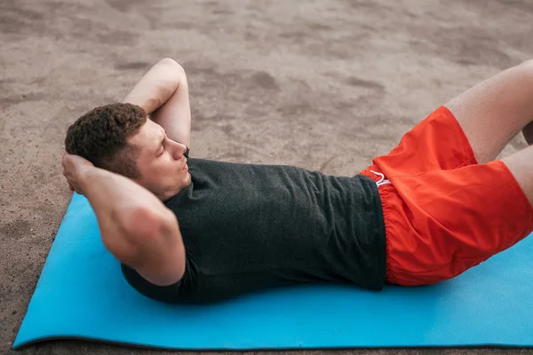 Young guy on rug. Trains twisting, abdominal muscles. Strengthening abdominal muscles. Raise torso. The concept of a healthy lifestyle or hobby. Man in the summer on the sports ground in the city.