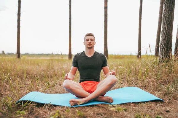 Young man guy sitting on a rug in lotus position. Practicing yoga in asana position. The concept of a healthy lifestyle or hobby. Reach nirvana, without stress. Summer forest.
