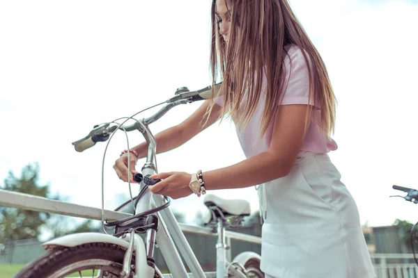 Ένα κορίτσι στέκεται με ένα ποδήλατο το καλοκαίρι στην πόλη. Στα χέρια της ένα κλείδωμα με κωδικό, κλείνει και προστατεύει τις μεταφορές κατά της κλοπής. Η έννοια της προστασίας από κλοπή και κλέφτες ποδηλάτων. — Φωτογραφία Αρχείου