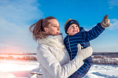 Küçük bir çocuk elini üste gösterir. Anne kucağında bebeği tutar. Kışın şehir.