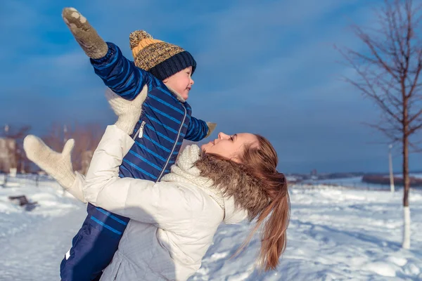 Een jonge moeder werpt een jongen zonen, vliegtuigen, spelen in de winter in de stad van frisse lucht. — Stockfoto