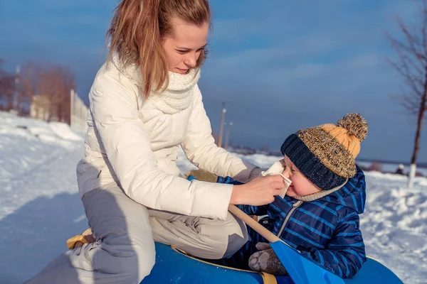 Eine junge Mutter wischt Rotz und sabbert an ihrem Knaben. Prävention der Grippebehandlung des Kindes im Freien im Winter an der frischen Luft, Krankheit und Erkältung. — Stockfoto