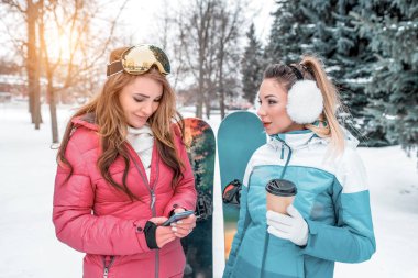 İki kız kız güzel kadınlar konuşurken mutlu snowboard arka plan. Resort, kışın doğada dinleniyor. Eller kupa sıcak çay ve kahve. Online sosyal ağlar bir ileti yazar.