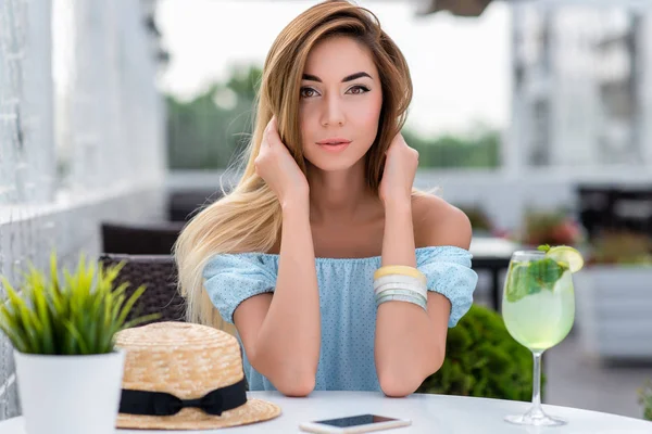 Mooi meisje in zomer café close-up weelderige haar. Zachte en sensuele blik in de ogen. Casual make-up gebruinde huid. Smartphone stro hoed, glas groene kalk drankje. Rusten na het werk op de veranda van restaurant. — Stockfoto