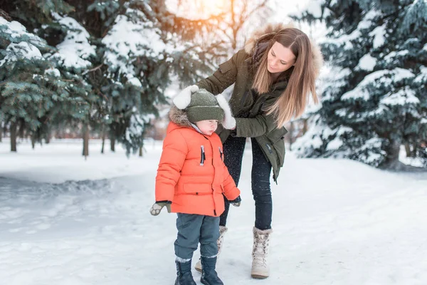 年轻的母亲女人摇掉了一个3-5岁的小男孩的雪帽, 儿子穿着冬衣。冬天, 在森林里的度假村里有很多雪。文本的可用空间. — 图库照片