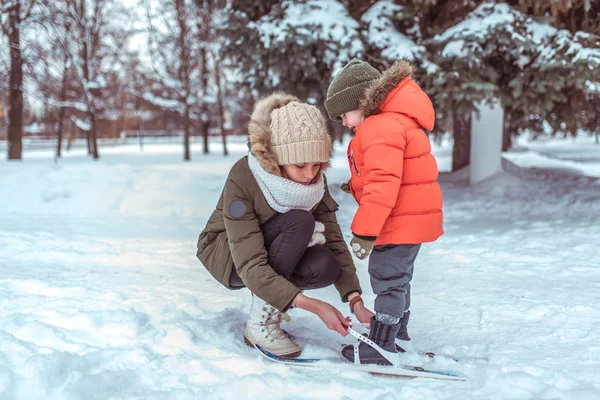 Junge Mutter schnallt kleinen Jungen im Alter von 3-5 Jahren an, Sohn in Winterkleidung. im Winter, im Waldgebiet, wo es viel Schnee gibt. Freiraum für Text. Betreuung und Sicherheit des Kindes in der Familie. — Stockfoto