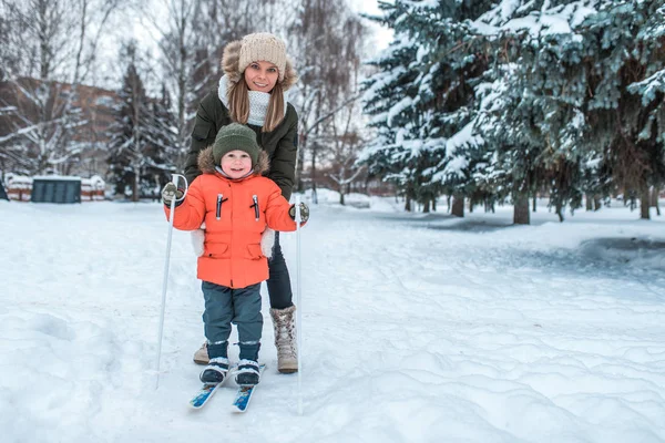 Young mother woman holds a little boy 2-3 years old, son in winter clothes. In the winter in the woods in the resort rest. Free space for text. Care and safety of the child in the family. — Stock Photo, Image