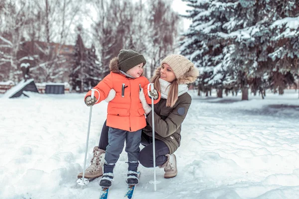 Ibu muda menggendong anak laki-laki berusia 3-5 tahun, anak laki-laki dengan pakaian musim dingin. Pada musim dingin di hutan di resor beristirahat. Ruang kosong untuk teks. Perawatan dan keselamatan anak dalam keluarga . — Stok Foto
