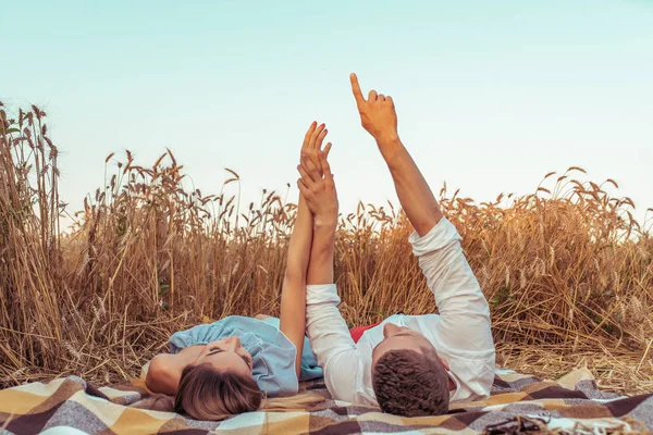 Una joven pareja, hombre y mujer, se encuentran con el atardecer y amanecen en verano en un campo de trigo. Acuéstese en la colcha en el suelo. Concepto de amor que cuida, abrazando la felicidad y el apoyo familiar. Las manos muestran las estrellas . — Foto de Stock